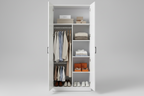 A tall white double-door wardrobe or closet with doors open, shown against a light gray studio background. Inside, the wardrobe is styled with hanging shirts and coats, folded towels and linens on shelves, orange shoe boxes, and several pairs of shoes at the bottom.