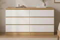 A modern 6-drawer dresser with white fronts and light oak wood trim, styled in a minimalist bedroom setting next to a bed and potted plant.