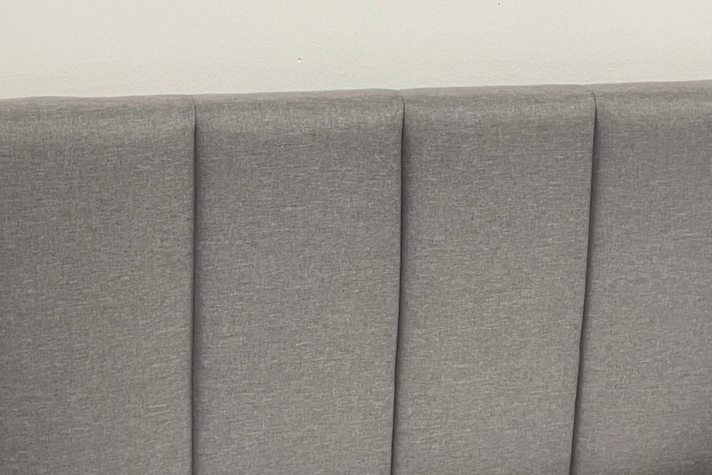 Gray upholstered headboard with pleated design on a plain background