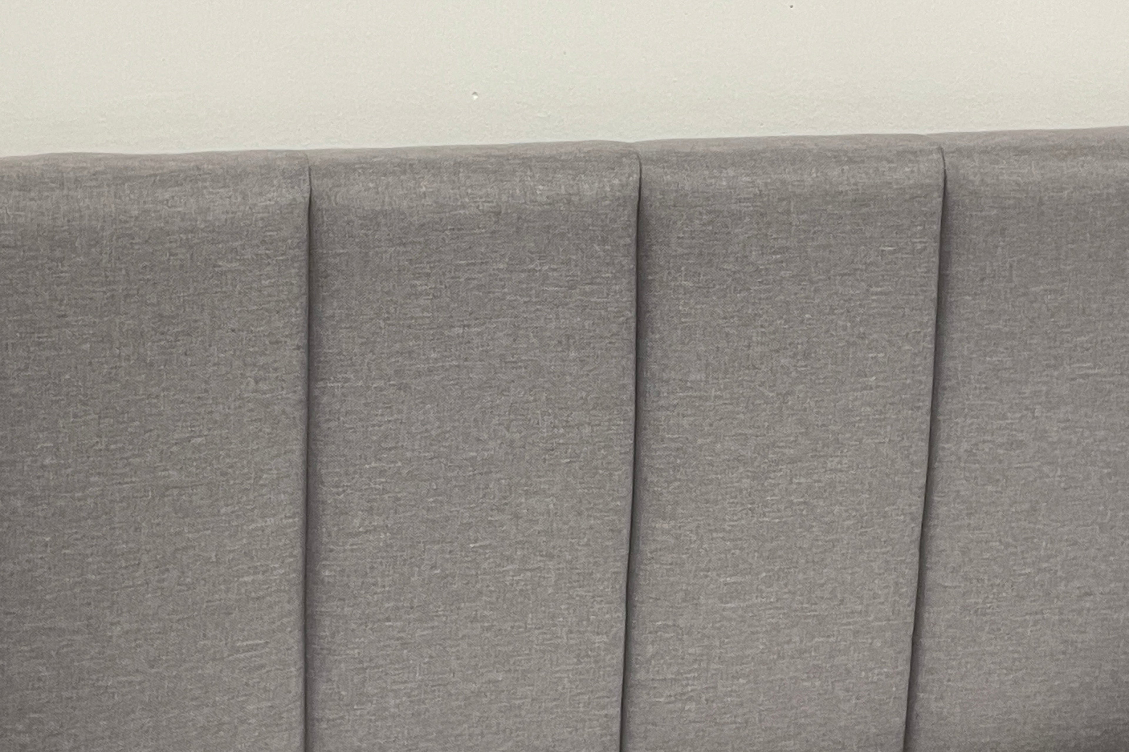 Gray upholstered headboard with pleated design on a plain background