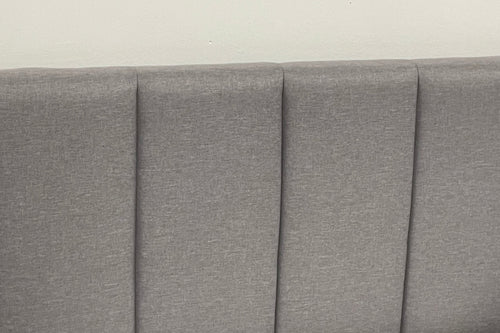 Gray upholstered headboard with pleated design on a plain background