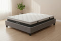 A Natural Story mattress on a gray upholstered bed frame, photographed on a clean light gray studio background.
