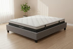 A Natural Story mattress on a gray upholstered bed frame, photographed on a clean light gray studio background.