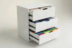 A white three-drawer nightstand or storage cabinet with pull-out drawer mechanisms partially extended, shown on a clean light beige studio background.