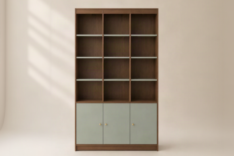 A tall wooden bookcase with three open shelves on the upper section and three pale sage green doors on the lower section, accented with small round gold knobs, set against a warm beige background.
