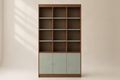 A tall wooden bookcase with three open shelves on the upper section and three pale sage green doors on the lower section, accented with small round gold knobs, set against a warm beige background.