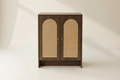 A walnut color cabinet with two doors featuring arched woven cane panels, set against a warm beige background.