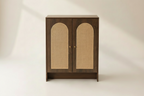 A walnut color cabinet with two doors featuring arched woven cane panels, set against a warm beige background.