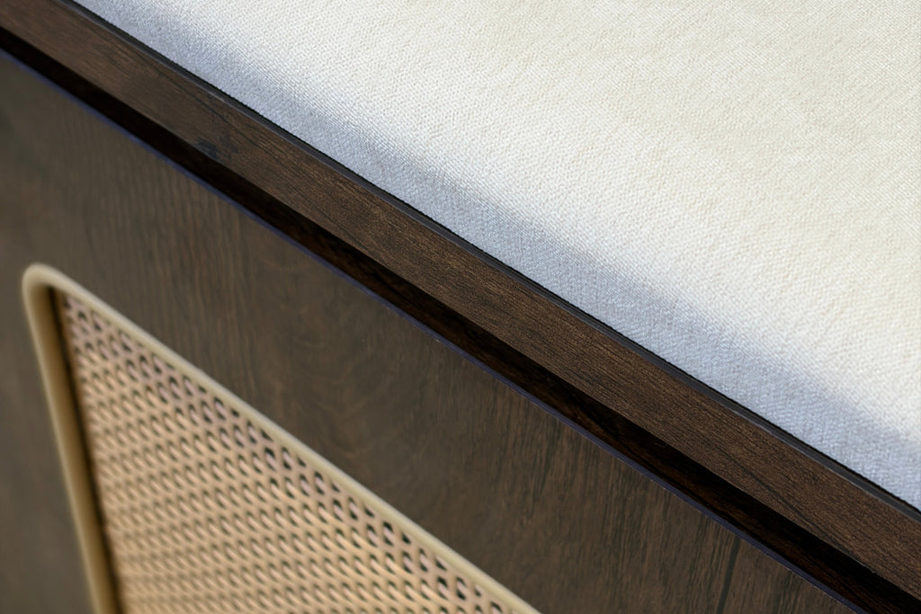 Close-up detail of a modern furniture piece featuring a dark wood cabinet base, a beige woven cane panel, and a light cream upholstered top surface.