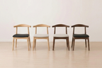 Four wooden chairs with leather and friable cushion seats arranged in a row on a light wooden floor.
