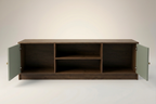 A modern wooden media console with a dark brown finish, featuring two sage green doors swung open to show the interior storage compartments, set against a clean light gray background.