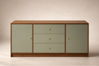 A mid-century modern sideboard cabinet with sage green doors and drawers, a warm brown wood frame, and small brass knobs, set against a neutral beige background.