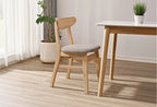 Wooden chair with gray cushion next to a wooden table in a room with a plant and curtains.