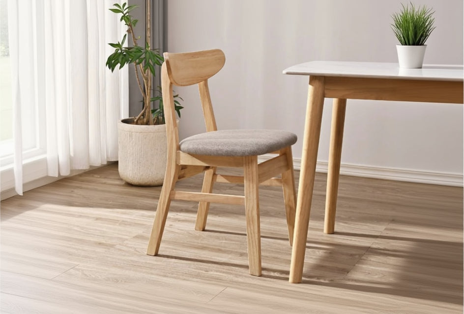 Wooden chair with gray cushion next to a wooden table in a room with a plant and curtains.