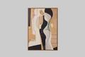 A framed abstract art print featuring a stylized female figure in black, beige, white, and light blue tones, hung on a warm off-white wall.