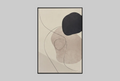 A framed abstract art print with organic shapes in beige, taupe, black, and soft pink tones, leaning against a light gray wall.