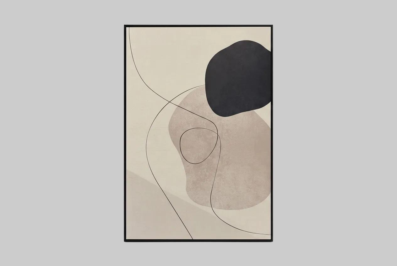 A framed abstract art print with organic shapes in beige, taupe, black, and soft pink tones, leaning against a light gray wall.