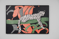 A framed art print featuring a stylized white spotted leopard with black spots, set against a background of large coral-pink and green abstract leaves on a black field, hung on a light gray wall.
