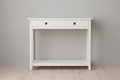 A white wooden console table with two drawers and a lower shelf, set against a neutral gray wall and light wood floor.