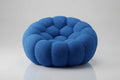 A modern, circular floor cushion or pouf in a textured blue fabric, featuring a segmented, scalloped outer edge and a tufted center, set against a light gray studio background.