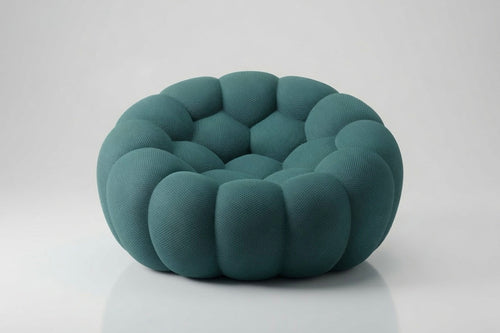A modern, low-profile circular pouf or accent chair upholstered in a textured teal fabric, featuring a segmented, bubble-like design, set against a clean light gray background.